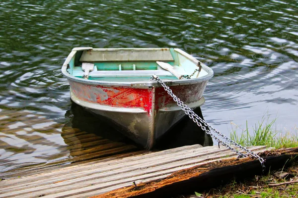 An aluminum row boat chained to the shore by a dock — Stock Photo, Image