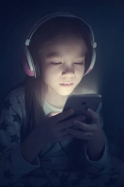 夜携帯電話とヘッドフォンの小さな女の子 — ストック写真