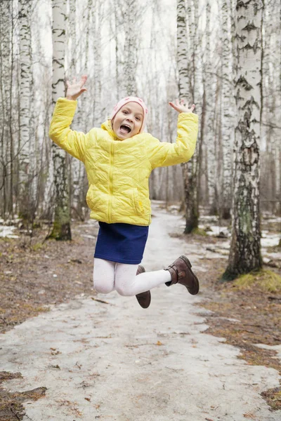穿着黄色夹克的女孩在春天的森林里跳跃着乐趣 — 图库照片
