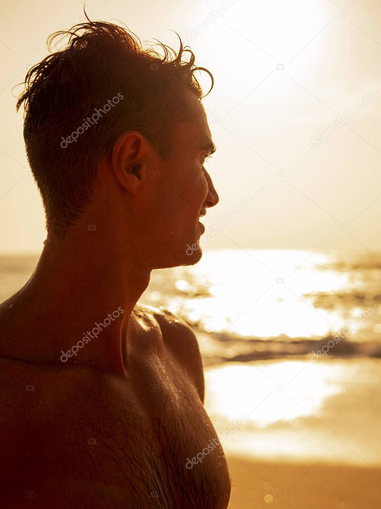 Portrait of a male athlete at sunset on the background of the beach and sea
