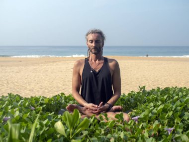 Kafasında rasta olan bir adam okyanus manzaralı plajda yoga yapıyor. Sri Lanka.