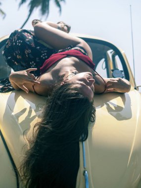 Genç bir kadın arabanın kaputunda güneşleniyor. Tatil, seyahat, plaj.
