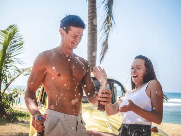 A man and a woman open a cola with splashes on the background of a car and the sea. Vacation, travel.