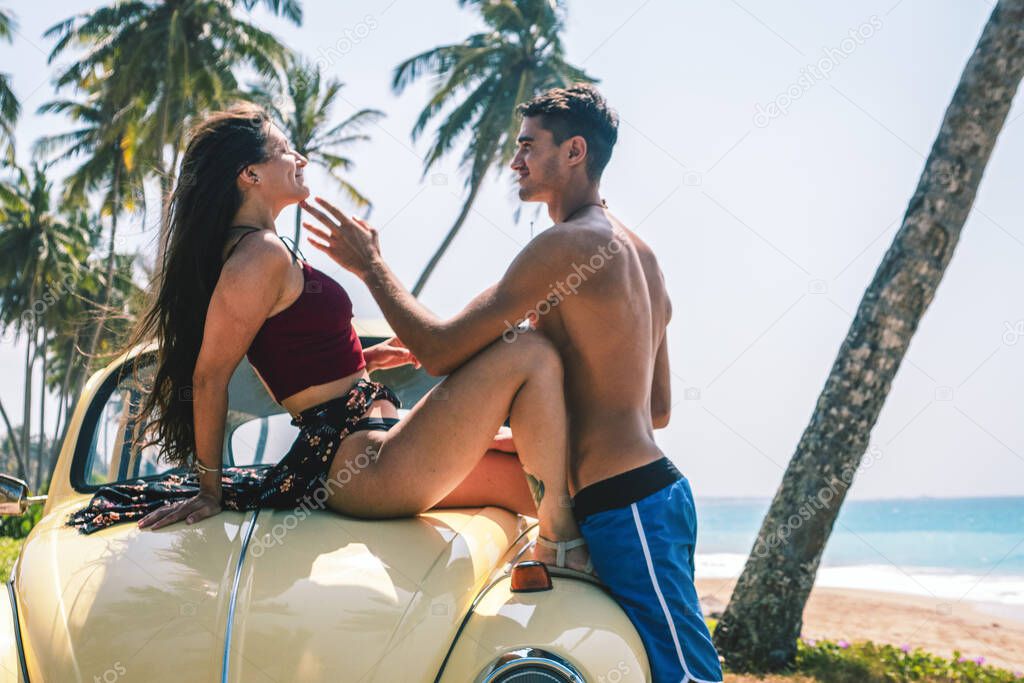 A man and a woman are flirting on the hood of a car. Love story. Vacation, travel, beach.