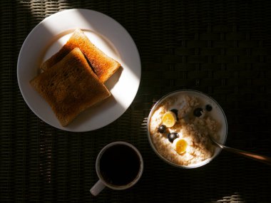 Kahvaltı sabah güneşiyle aydınlatılır. Kahve, tost ve yulaf ezmesi. Masadaki üst görünüm