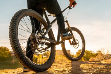 Dağ bisikletli adam. Bisiklet tekerleri gün batımında görüntüyü kapatır. Dağ bisikleti süren bisikletçinin alçak açılı görüntüsü. Ayağını pedala koy..