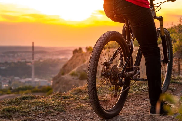 日落时骑着一辆现代越野车坐在城市后面山上的山地自行车的背影. — 图库照片