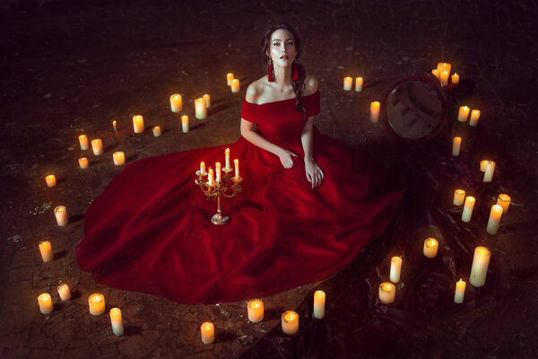 Beautiful lady dressed in red ball gown sitting with candles
