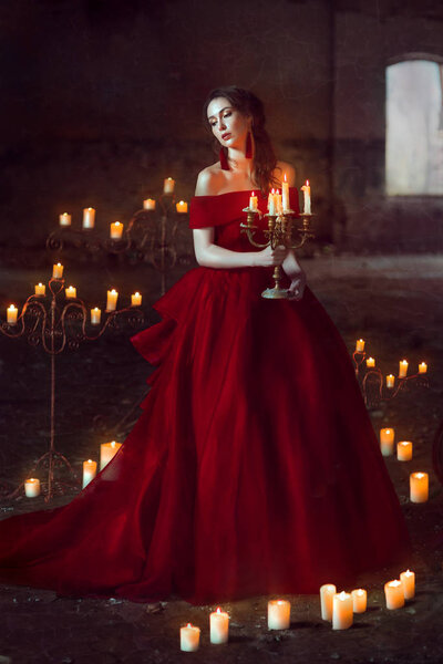 Beautiful lady dressed in red ball gown sitting with candles