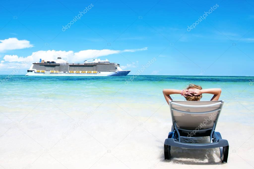 Cruise vacation concept. Cruise ship in the sea near the tropical island with woman lying on a beach bed near the sea. Relaxing and enjoying vacation.