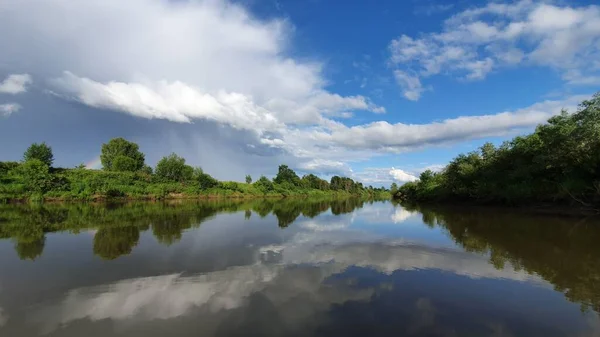 white clouds in the blue sky over a calm river