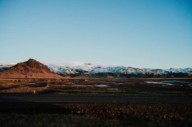 İzlanda'daki bir manzara bir yol ve gün batımında arkasında bazı dağ.
