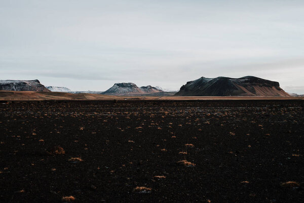 Вулканическое поле в Исландии на закате с несколькими горами на заднем плане
.