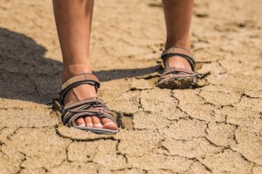 Kız Sandaletler içinde Kuru kum üzerine gider. Detay.