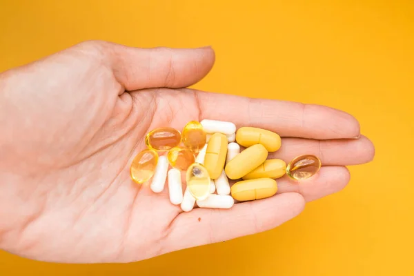 Sarı arka planda hapları olan insan eli. Renkli kompozisyon