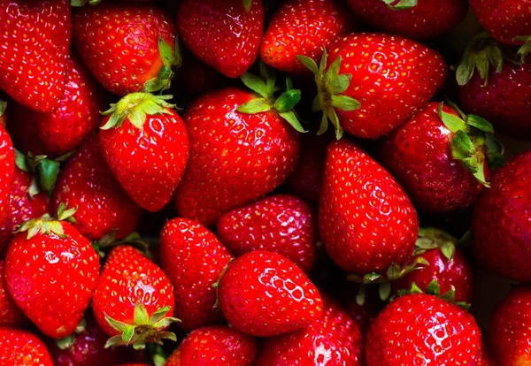 Red biological strawberry background. Many bright fresh berries with green leaves. Horizontal harvesting composition. Seasonal fruits wallpaper. Raw food pattern. Vitamins and healthy eating products.