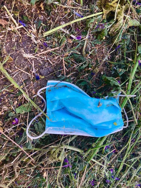 Used blue medical mask thrown in the park. Dirty surgical mask lies on the ground and grass. Medical waste disposal problem. Hygienic mask during a pandemic of corona virus. Environmental pollution