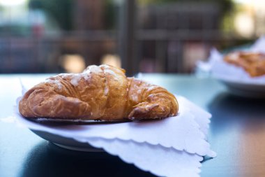 İtalyan kahvaltısı. Dışarıdaki terasta beyaz peçetelerin üzerinde sunulan taze kruvasan ya da kornet arka plandaki komşu eve açıktır. Yaz sabahı fırını. 