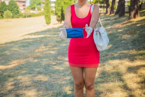 Medische masker en witte handschoenen in het dagelijks leven. Zomer dag na quarantaine realiteit. Vrouw in roze jurk toont een handgemaakte blauwe chirurgische beschermende masker. Ik moest maskers dragen. Zomer in het park — Stockfoto