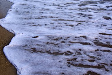 Dalgada beyaz köpük, ıslak kıyıda