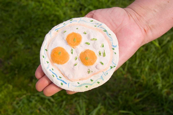 child pottery in the from of fried eggs, in the hand, outdoors