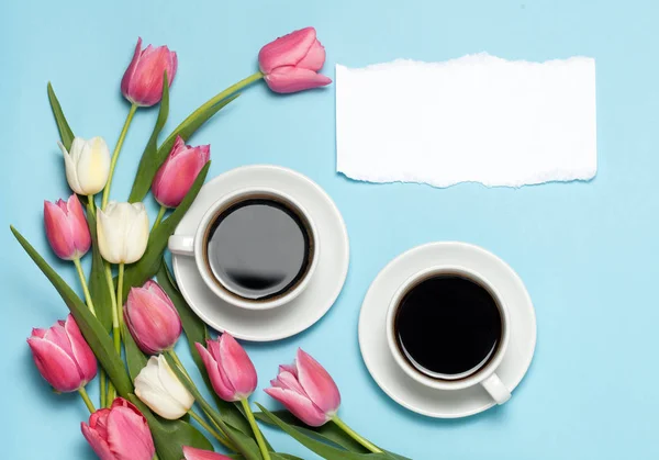Дві чашки кави і рожеві тюльпани на синьому фоні . — стокове фото