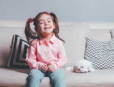 Rahat giyen oyuncak köpek ve gülümseyen ile kanepede oturan içinde oldukça mutlu küçük kız.