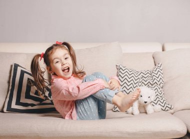 Rahat giyen oyuncak köpek ve gülümseyen ile kanepede oturan içinde oldukça mutlu küçük kız.