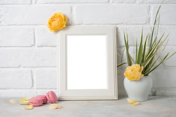Resim çerçevesi mockup macaroons ve beyaz tuğla zemin üzerine sarı güllerle süslenmiş. metin için boş yer