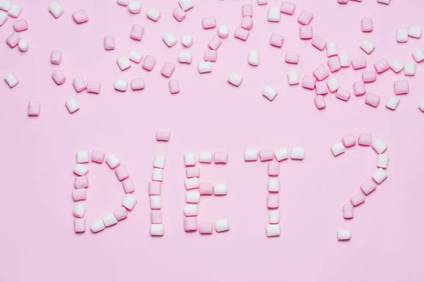 Pink and white Marshmallows on pink background with word diet. Top view, flat lay. Concept of not healhy eating and diets