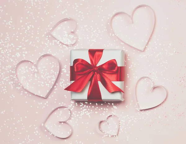 Caja de regalo y corazones de papel con brillo brillante sobre fondo rosa. San Valentín romántico concepto de saludos. Vista superior, plano — Foto de Stock