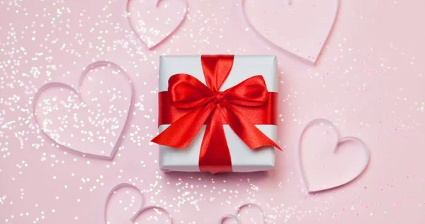 Caja de regalo y corazones de papel con brillo brillante sobre fondo rosa. San Valentín romántico concepto de saludos. Vista superior, plano — Foto de Stock