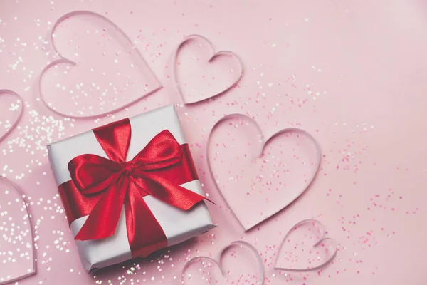 Caja de regalo y corazones de papel con brillo brillante sobre fondo rosa. San Valentín romántico concepto de saludos. Vista superior, plano — Foto de Stock