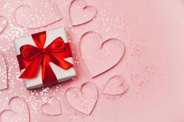 Caja de regalo y corazones de papel con brillo brillante sobre fondo rosa. San Valentín romántico concepto de saludos. Vista superior, plano — Foto de Stock