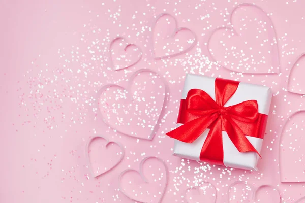 Caja de regalo y corazones de papel con brillo brillante sobre fondo rosa. San Valentín romántico concepto de saludos. Vista superior, plano — Foto de Stock