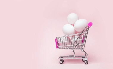 Pembe arka planda paskalya yumurtası dolu bir alışveriş arabası. Yaratıcı Paskalya konsepti.