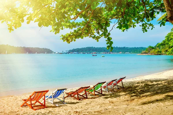 Camas de sol multicoloridas em uma praia de areia na sombra. Uma manhã quente nos trópicos . — Fotografia de Stock