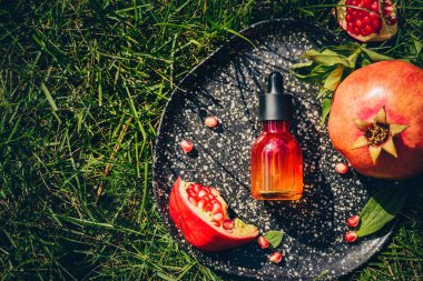 Nar tohumu yağı, cam şişedeki serum dekoratif rende, yeşil çimen arka planında. Düzlük, minimalizm. Yaşlanmayı önleyen organik cilt bakımı kavramı.