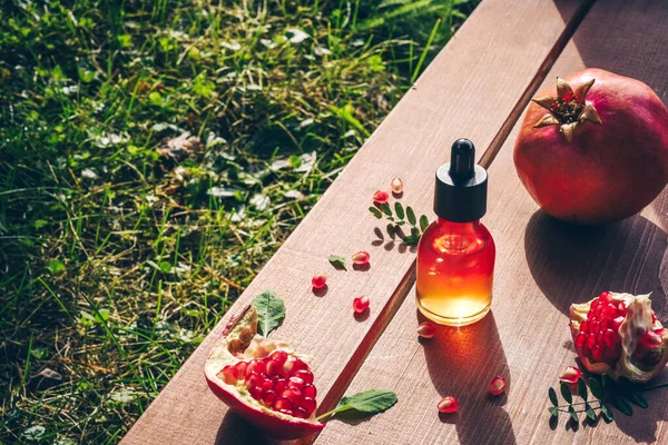 Trendy sunlight pomegranate seed oil, serum in glass bottle on wooden background. Lifestyle Concept of anti-aging skin care.