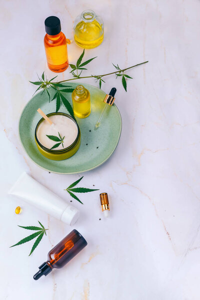 Косметика с марихуаной на бирюзовой пластине на светлом мраморном фоне. Копирование пространства, макет
.