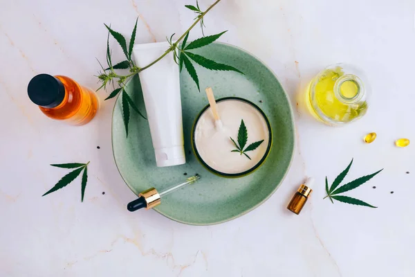 Cosmetics with cannabis oil on a turquoise plate on a light marble background. Copy space, mockup. — Stock Photo, Image