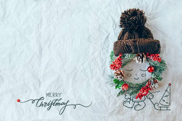 Christmas concept. Cute baby made of wreath of evergreen spruce, knitted hat and illustration on a white background. Minimal winter vacation idea. Flat lay top view composition. — Stock Photo, Image