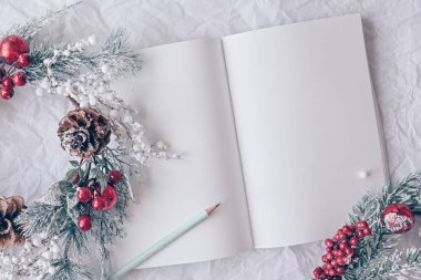 Noel konsepti. Noel süslemeli beyaz defter, beyaz arka planda çelenk. Minimum kış tatili fikri. Düz görünüm bileşimi yatıyordu.