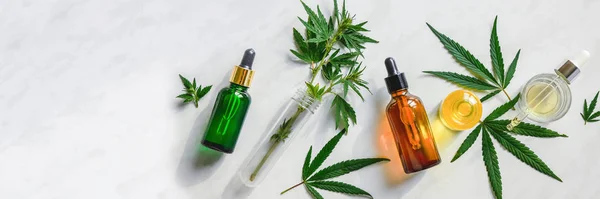 Várias garrafas de vidro com óleo de CBD, tintura de THC e folhas de cânhamo em um fundo de mármore. Deitado plano, minimalismo. Óleo de CBD de cosméticos . — Fotografia de Stock