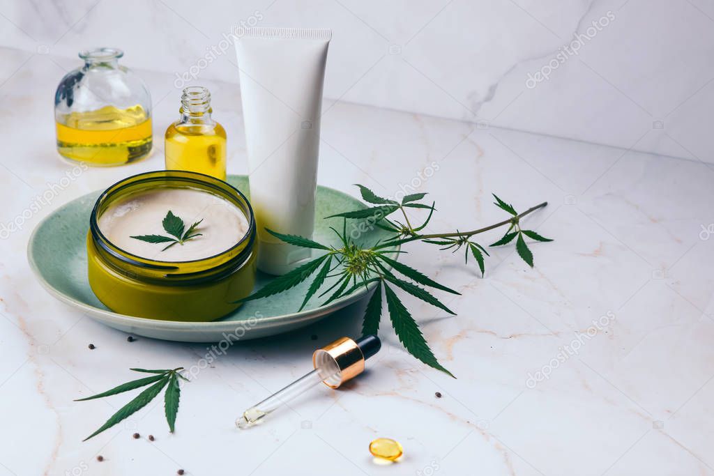Cosmetics with cannabis oil on a turquoise plate on a light marble background. Copy space, mockup.