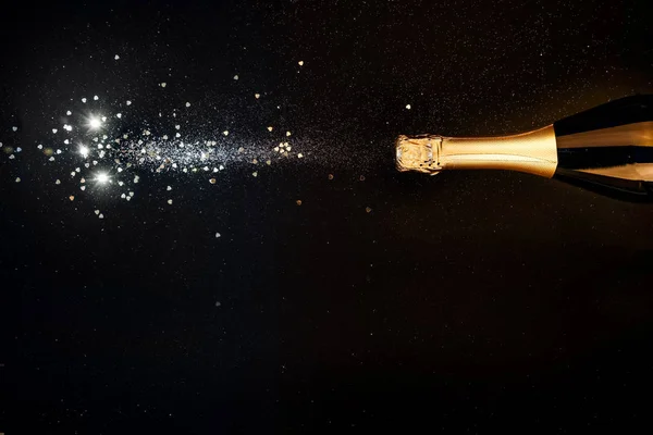 Champagnerflasche mit Goldspritzern, glitzert auf schwarzem Grund. flach lag. Minimale Weihnachtsfeier Konzept kopiert Raum — Stockfoto