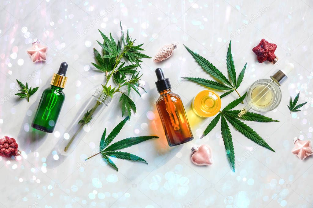 Glass bottles with CBD oil, hemp leaves In Christmas decoration. Festive background for cannabis Flat lay