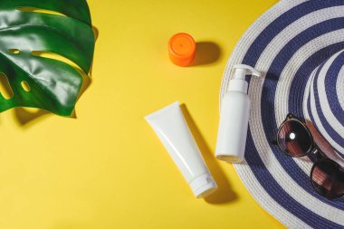 Güneş koruma nesneleri. Sarı arka planda şapka, güneş gözlüğü ve koruma kremi. Plaj aksesuarları. Yaz Konsepti