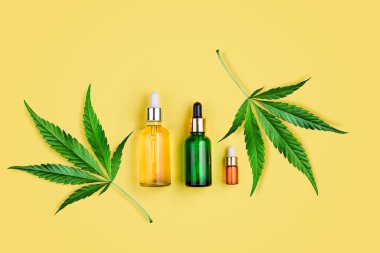 Cbd yağlı cam şişeler, THC tentür, sarı arka planda kenevir yaprakları. Düzlük, minimalizm. Kozmetik Cbd kenevir yağı