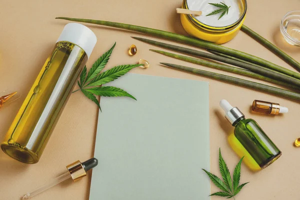 Cosméticos com óleo de cânhamo CBD em um fundo bege, caderno, folhas de maconha. Espaço de cópia, mockup — Fotografia de Stock